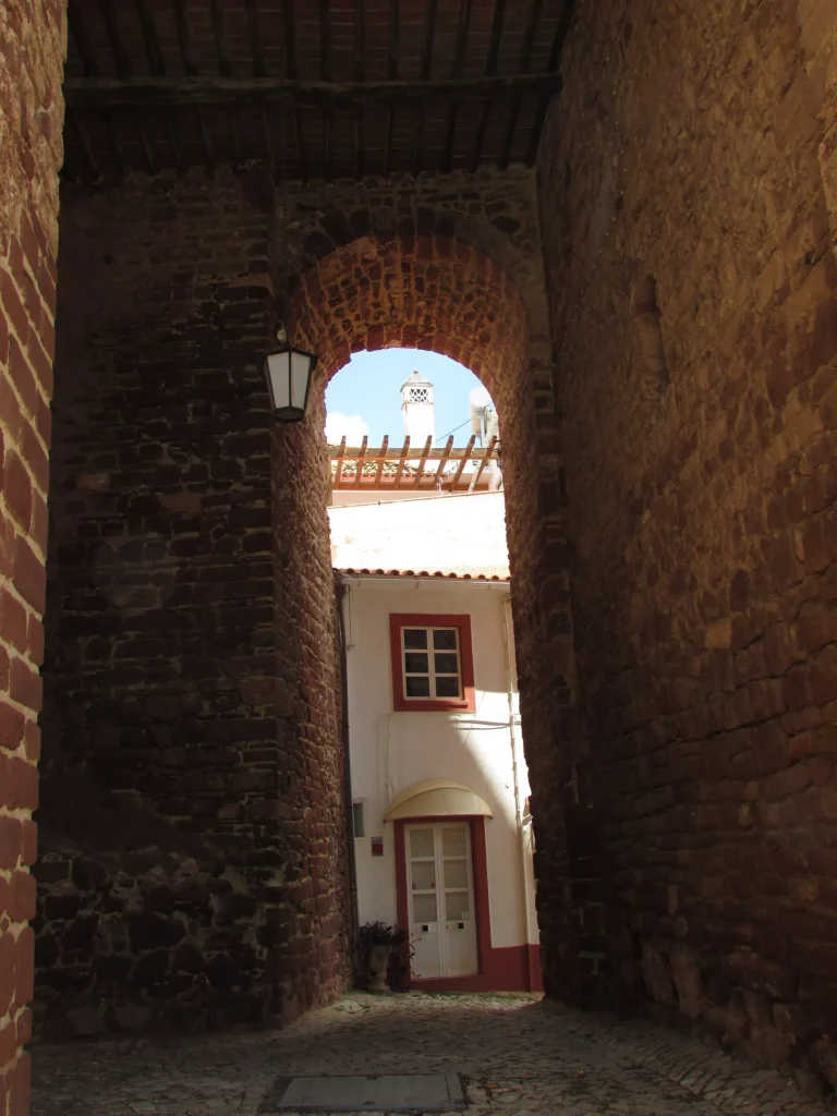 Medieval city gate of Silves built in reddish stone, seen from street level.